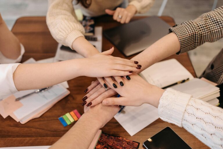 Hands stacked in teamwork gesture over a table with office items symbolizing collaboration.