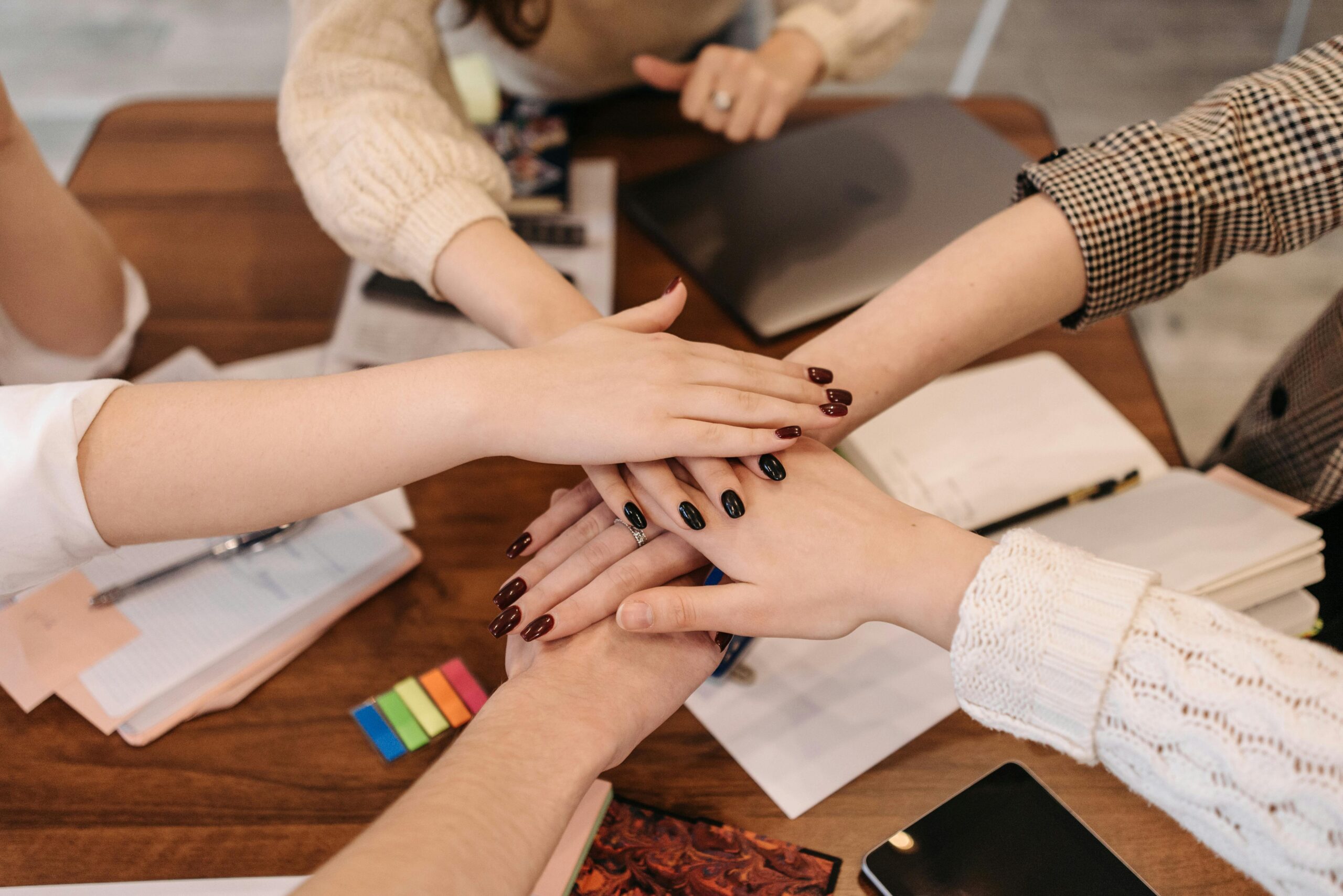 Hands stacked in teamwork gesture over a table with office items symbolizing collaboration.